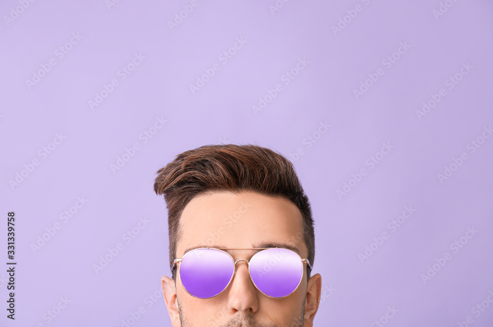 Young man with stylish sunglasses on color background