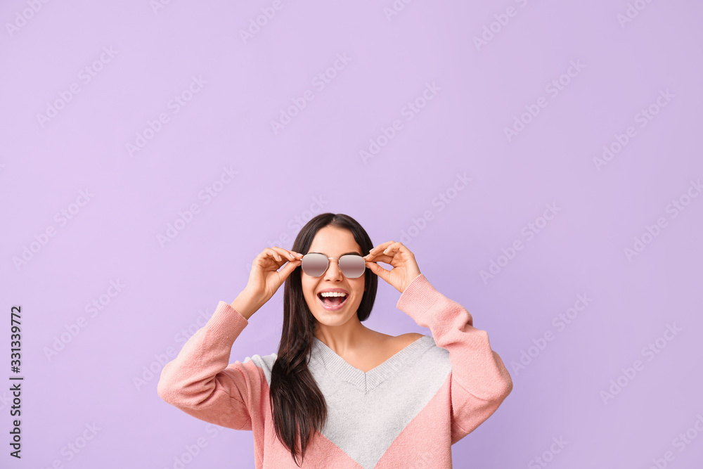 Young woman with stylish sunglasses on color background