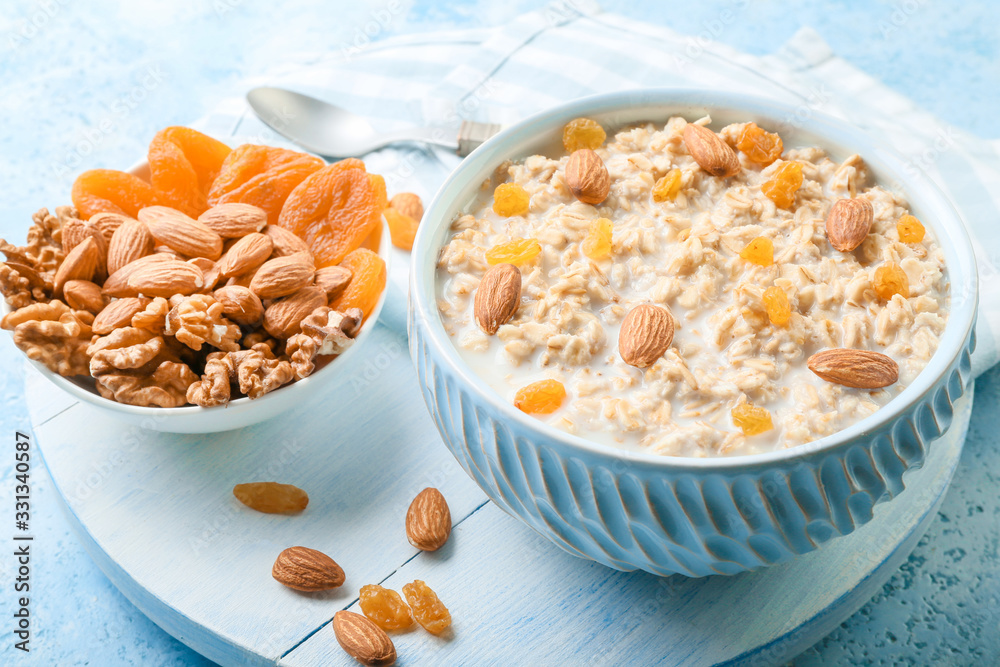 Bowls with tasty sweet oatmeal, dry apricot and nuts on color background