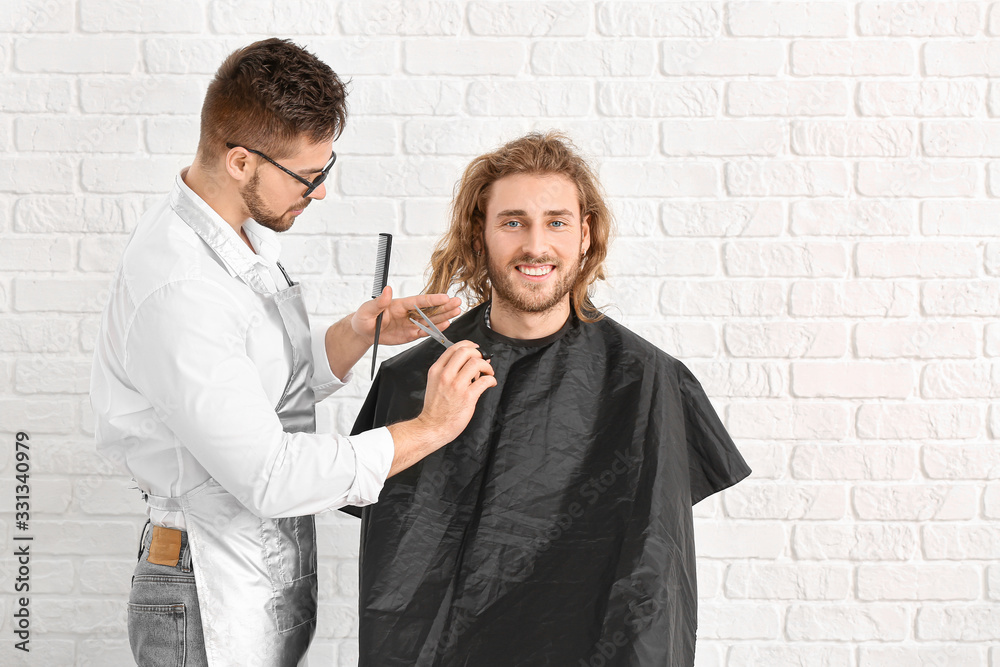 Young hairdresser working with client against white brick background