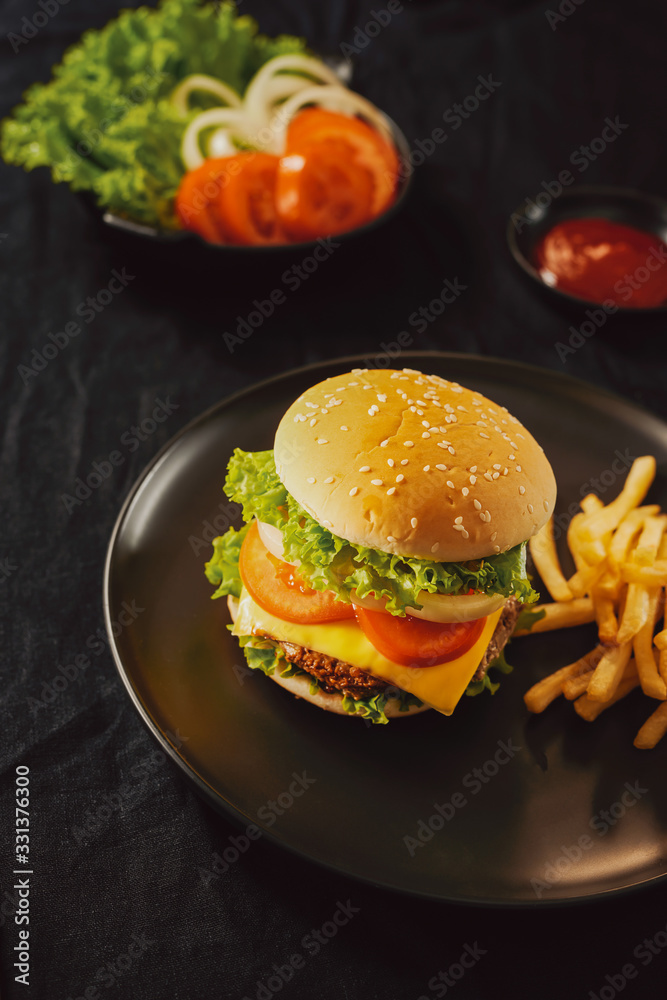 Fresh Tasty burger on cutting board with with french fries, ketchup and cola in glass over black bac