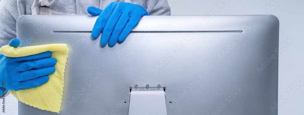 Young woman housekeeper in apron is cleaning silver computer surface with blue gloves, wet yellow ra