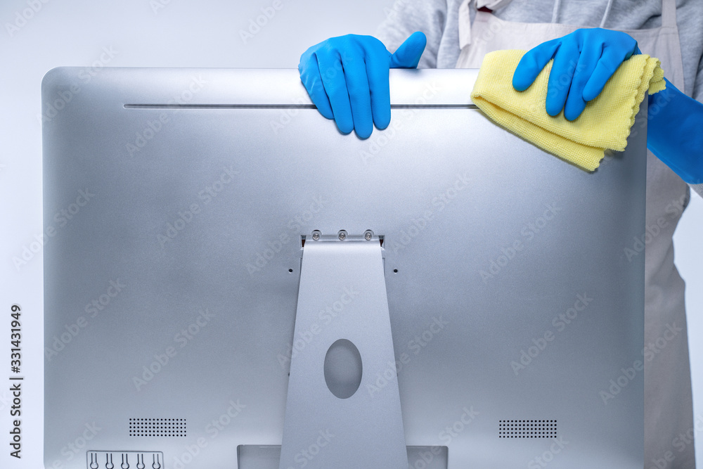 Young woman housekeeper in apron is cleaning silver computer surface with blue gloves, wet yellow ra