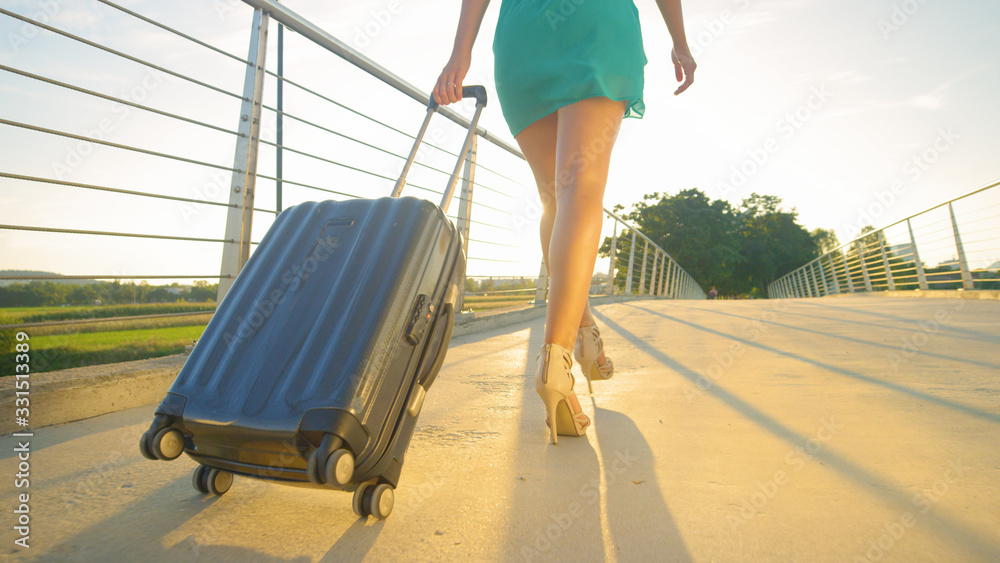 LOW ANGLE: Young woman in green sundress and high heels walks to the airport