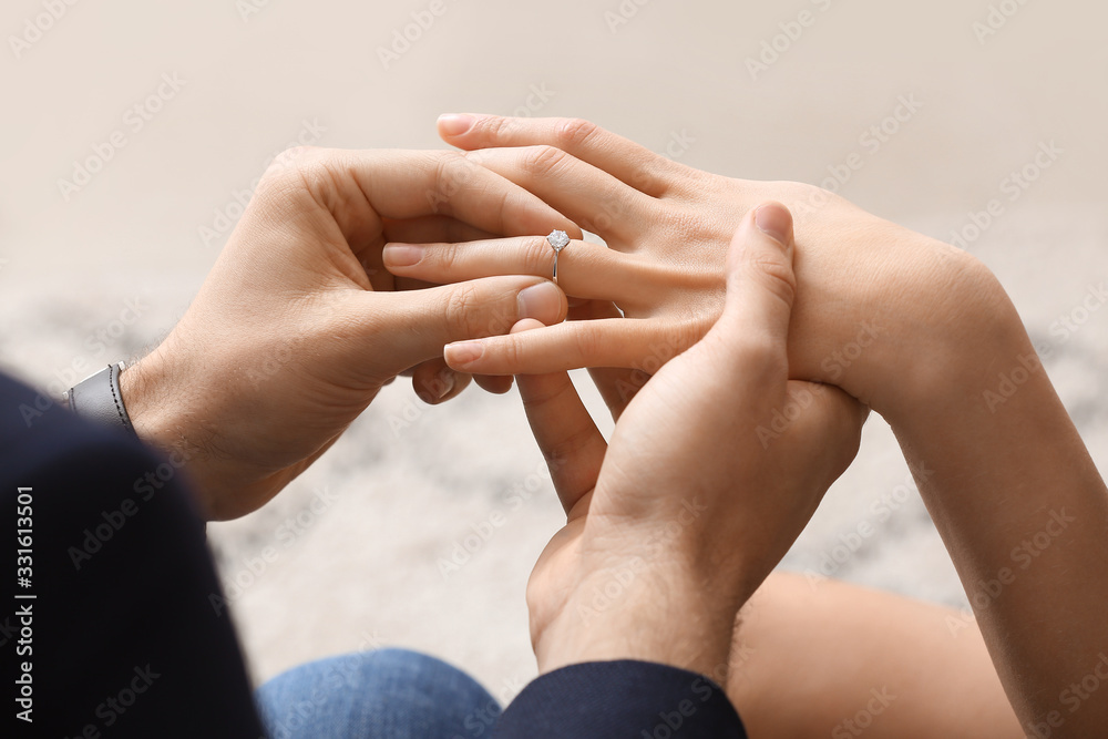 Young man putting ring on finger of his fiancee after marriage proposal, closeup