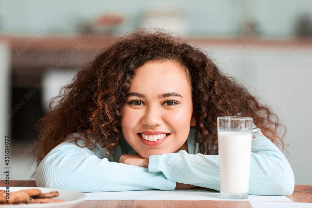 Young African-American woman with milk in kitchen