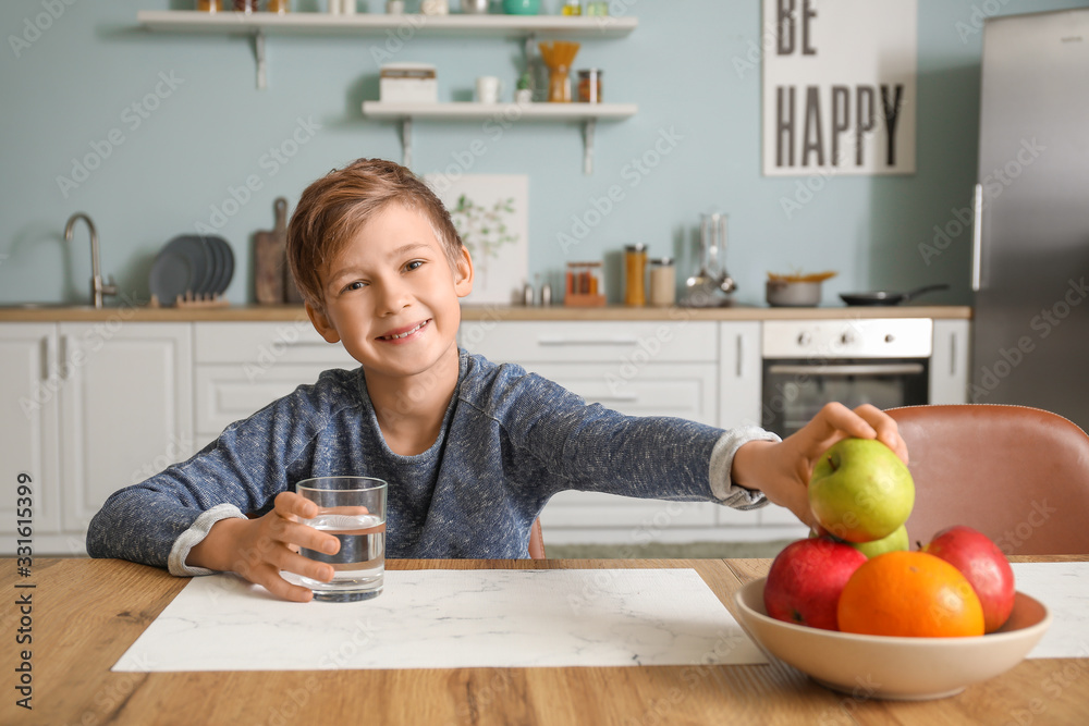 Cute little boy eating apple and drinking water in kitchen