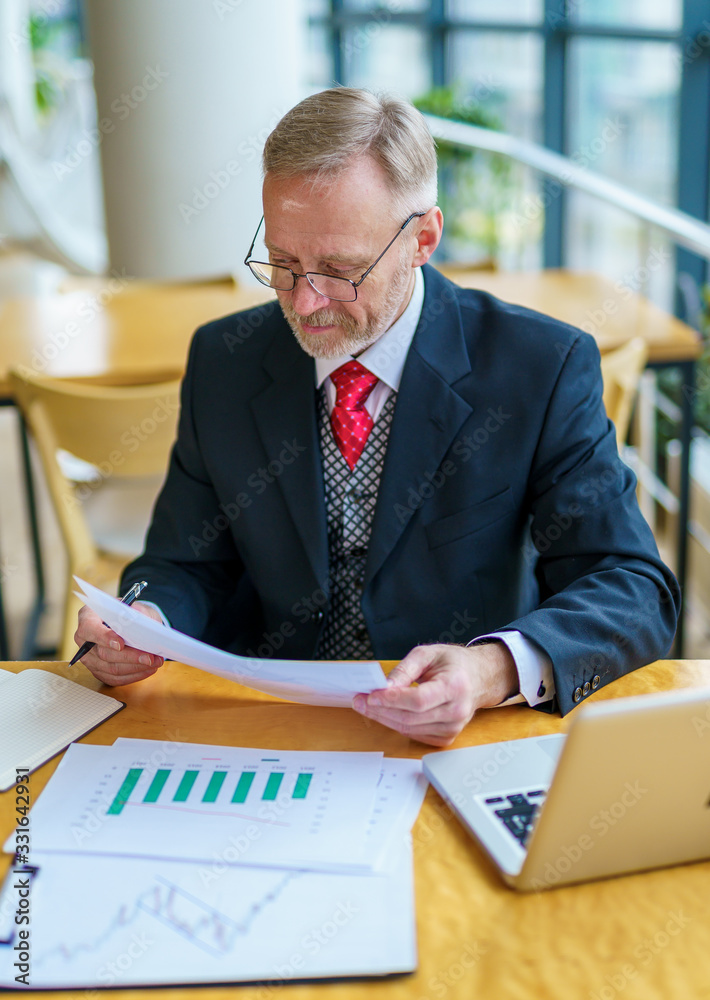 Thoughtful businessman is reading important business papers. Photo in front of the window with city 