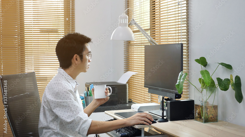 Asian freelancer working from home and using computer while drinking a coffee