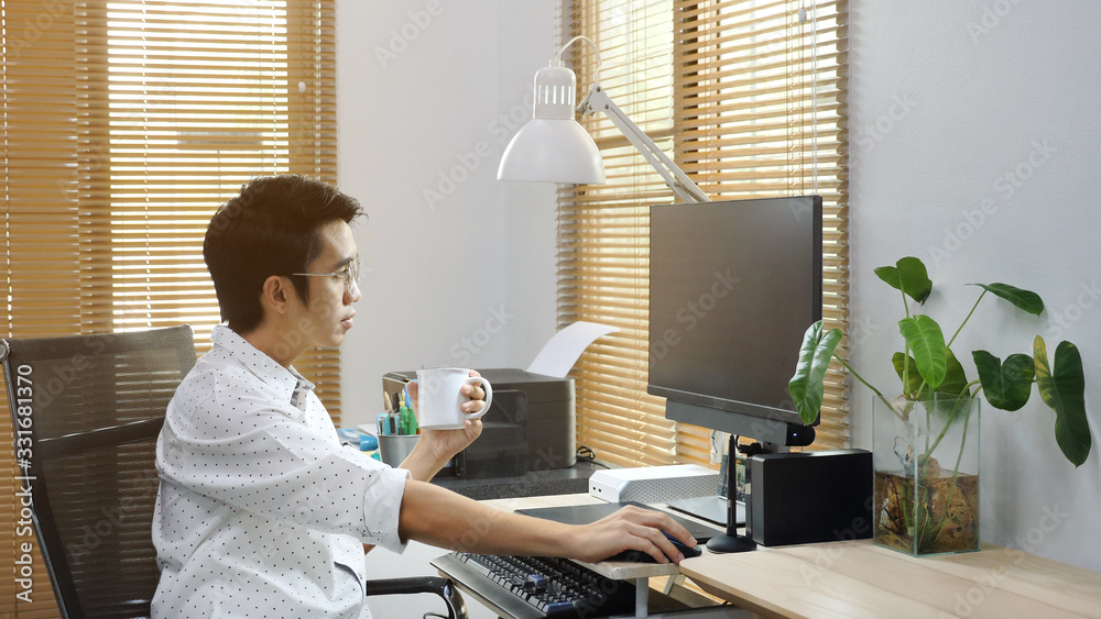 Asian freelancer working from home and using computer while drinking a coffee