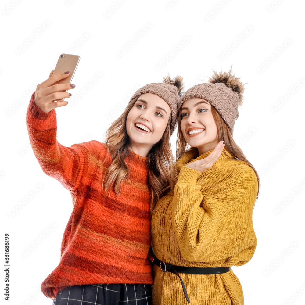 Young women in warm sweaters taking selfie on white background