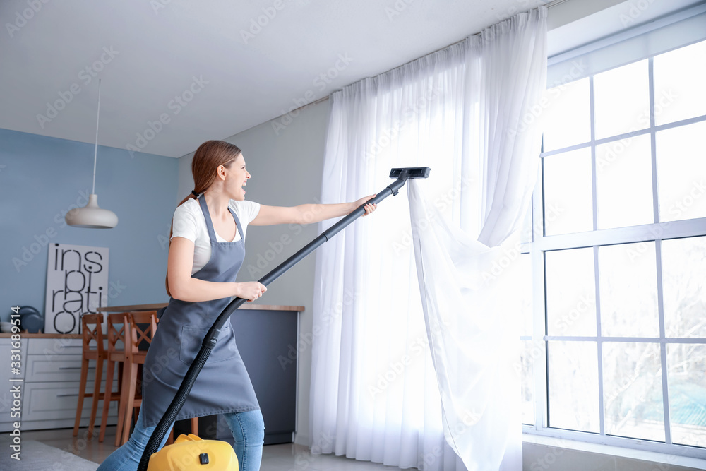 Afraid young woman with sucked into vacuum cleaner curtain at home