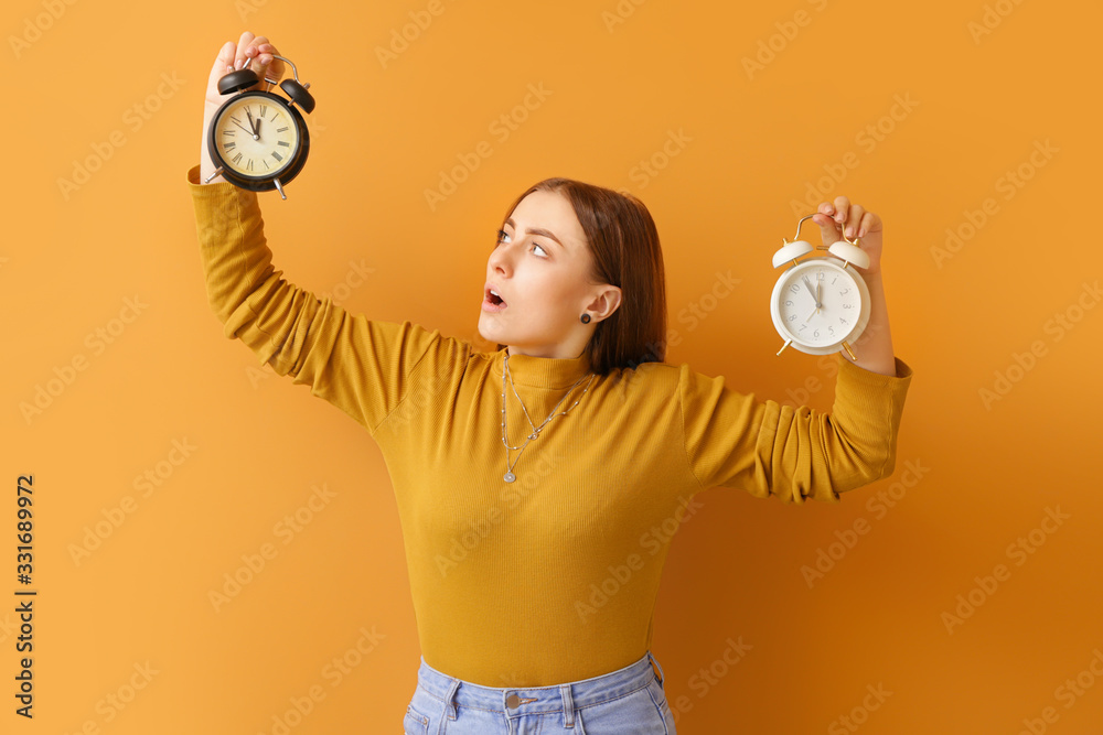 Shocked young woman with alarm clocks on color background