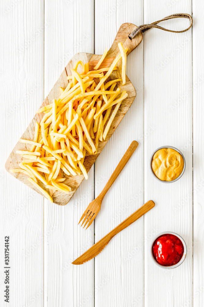 French fries served on cutting board on white wooden table top-down