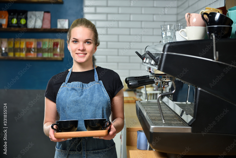 The bartender of the barista, a young girl in a coffee shop holds in her hands two mugs of coffee an