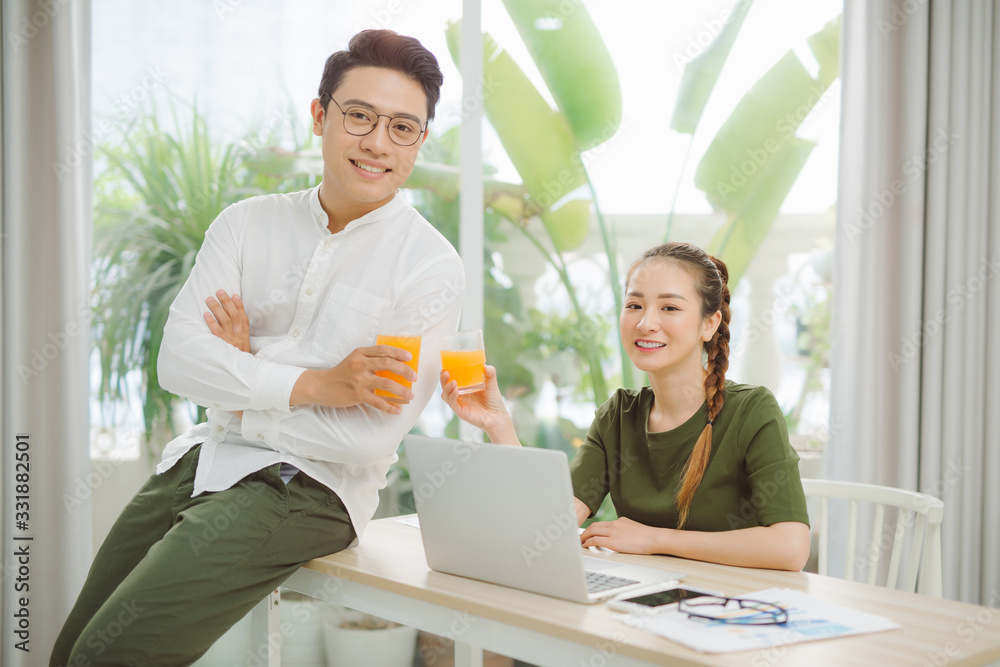 Happy young couple holding glasses of orange juice at the living room and looking to each othe