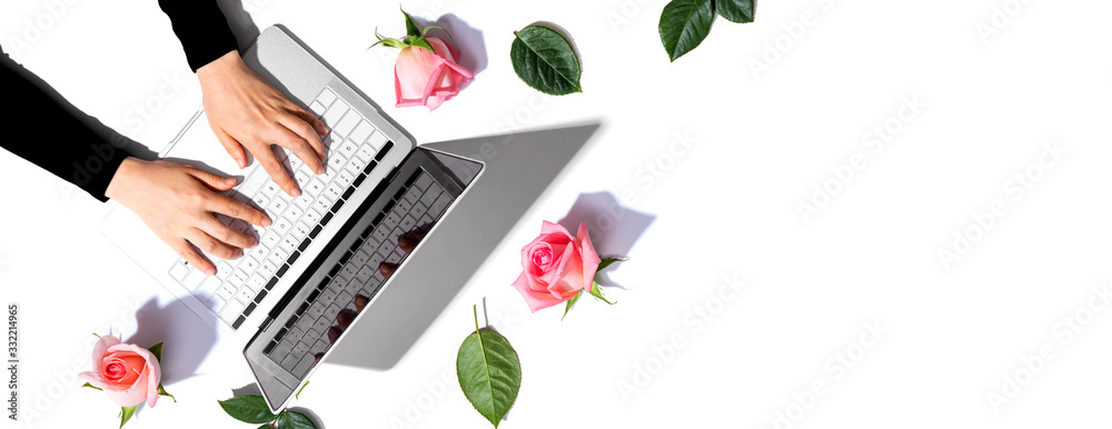 Woman using her laptop with pink roses - flat lay