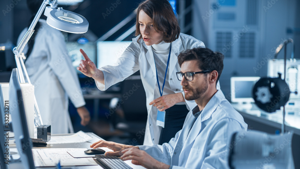 Machine Engine Development Engineer Working on Computer at His Desk, Talks with Female Project Manag