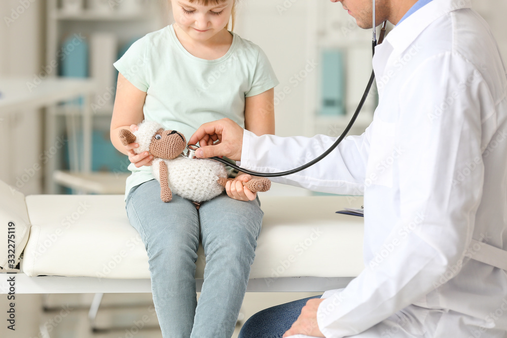 Pediatrician with toy showing little girl how to use stethoscope in clinic