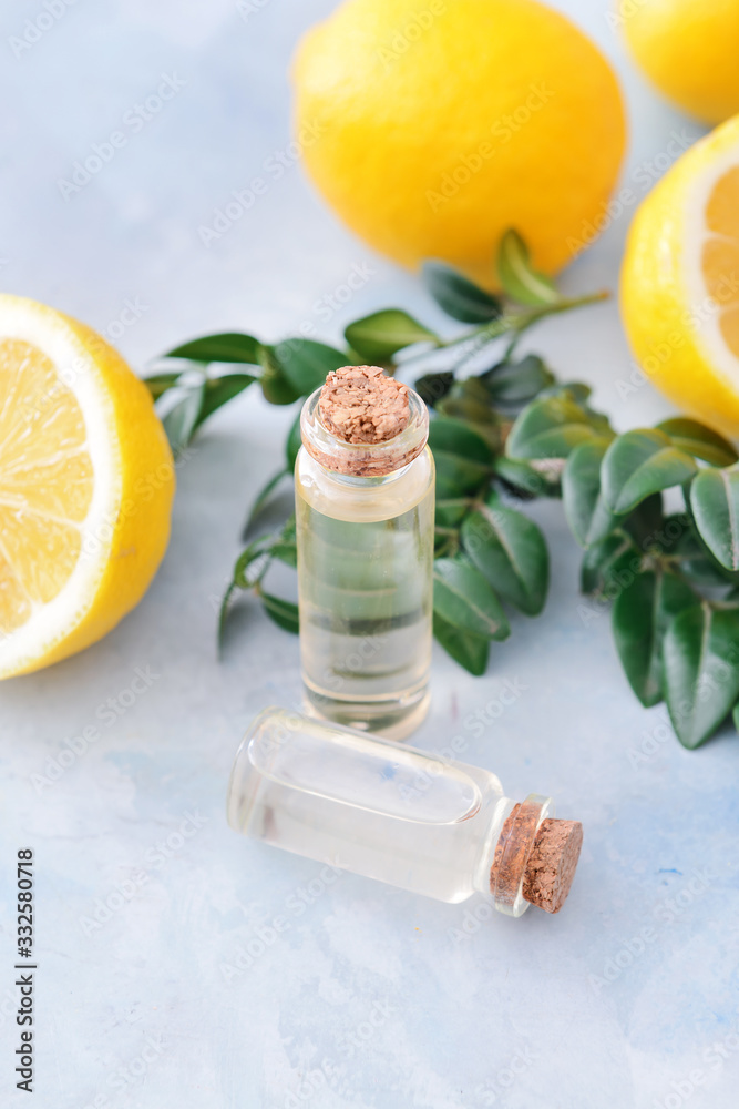 Bottles with lemon essential oil on color background