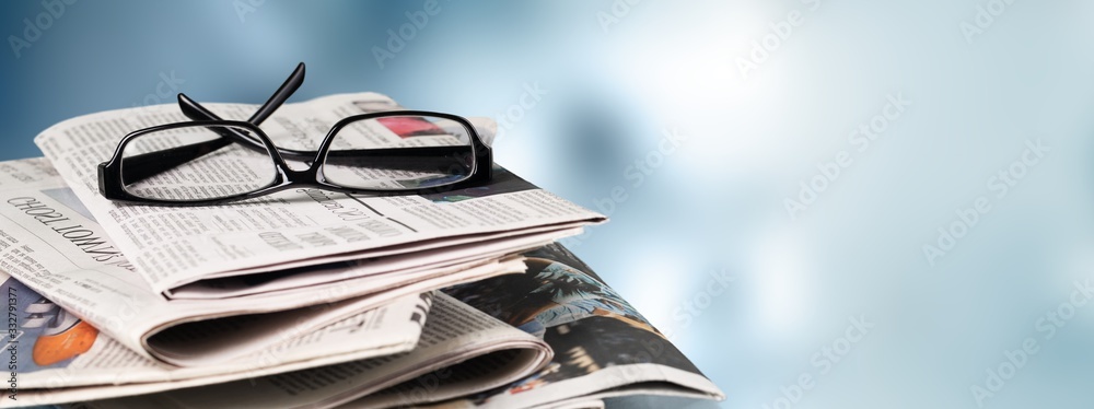 Pile of newspapers stacks and glasses on blur background