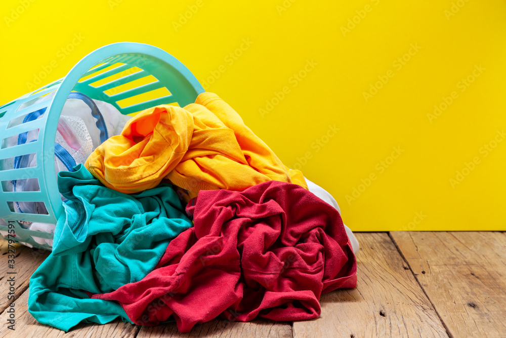 Pile of dirty laundry in washing basket on wooden plank yellow background.