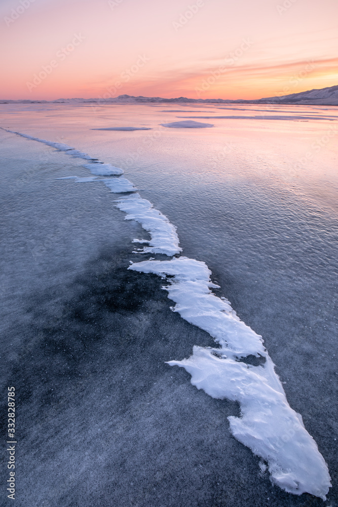 Frozen winter landscape of ice on lake Baikal during a colorful sunset. Lake Baikal, Siberia, Russia