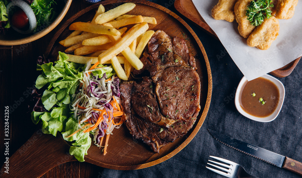 Pork steak grilled on a wooden plate with vegetables and french fries