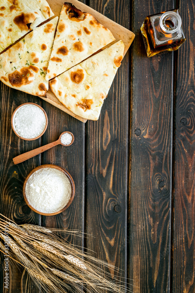 Focaccia ingredients. Wheat ears, flour, oil near bread on dark wooden background top-down copy spac