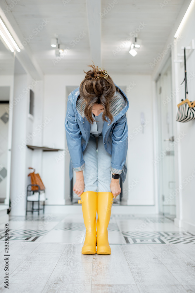 Woman wearing yellow boots and raincoat at the hallway of the apartment. Rainy weather concept