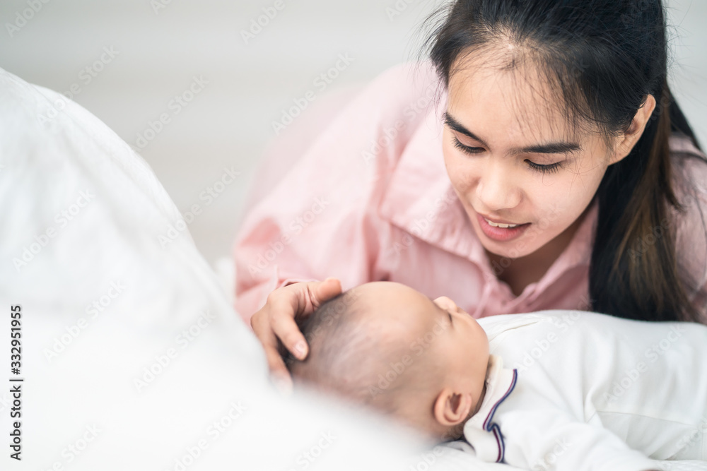 亚洲年轻的母亲和婴儿一起在可爱的家里的卧室里。女人抚摸着小婴儿的头。Gi