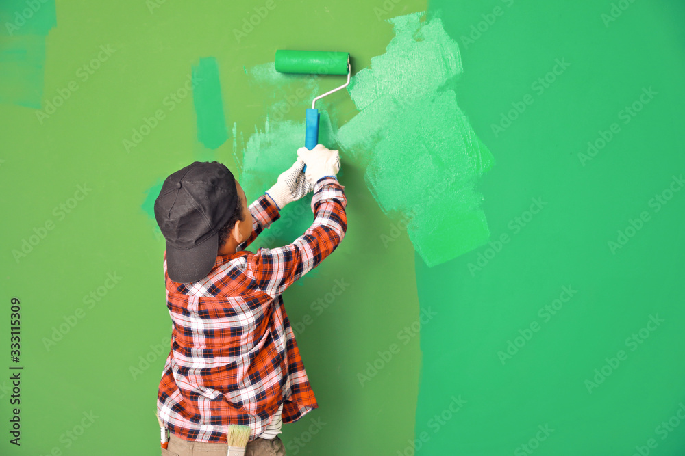 Little African-American boy painting wall in room