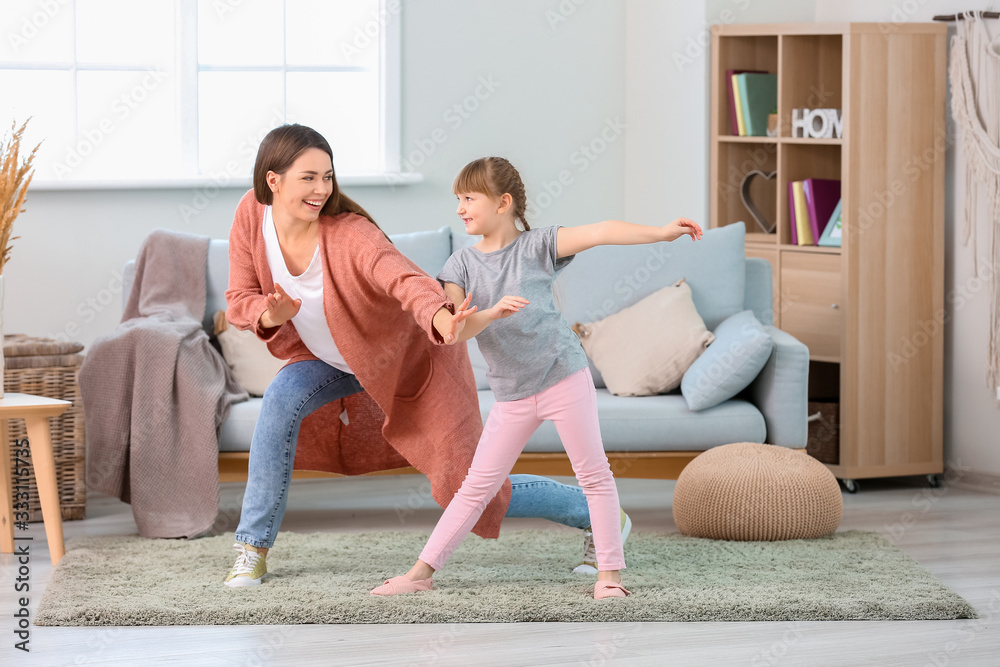 Happy mother and her little daughter dancing at home