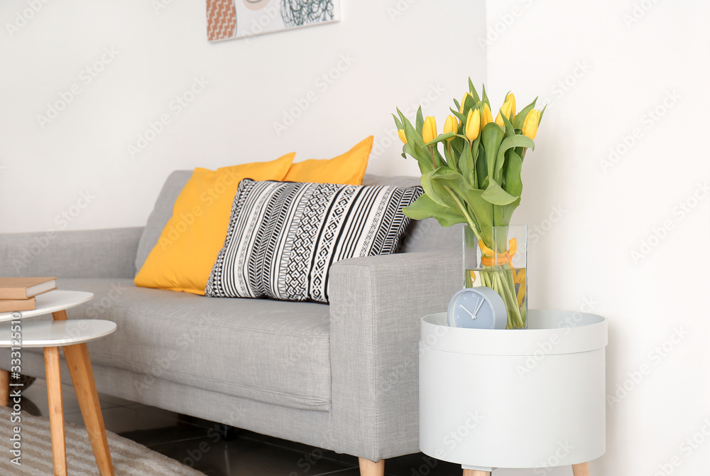 Interior of modern room with comfortable sofa and table with spring flowers