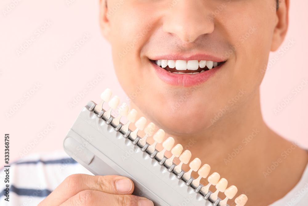 Man with teeth color samples on color background, closeup