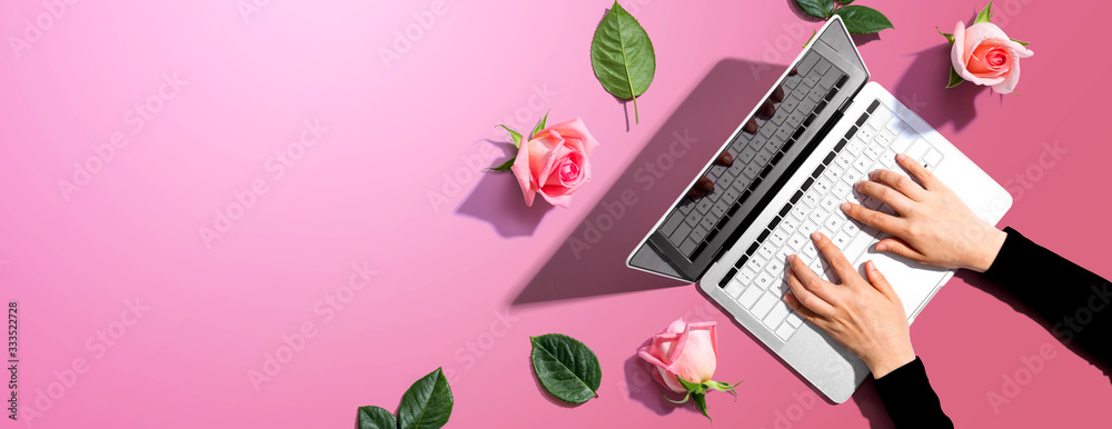 Woman using her laptop with pink roses - flat lay