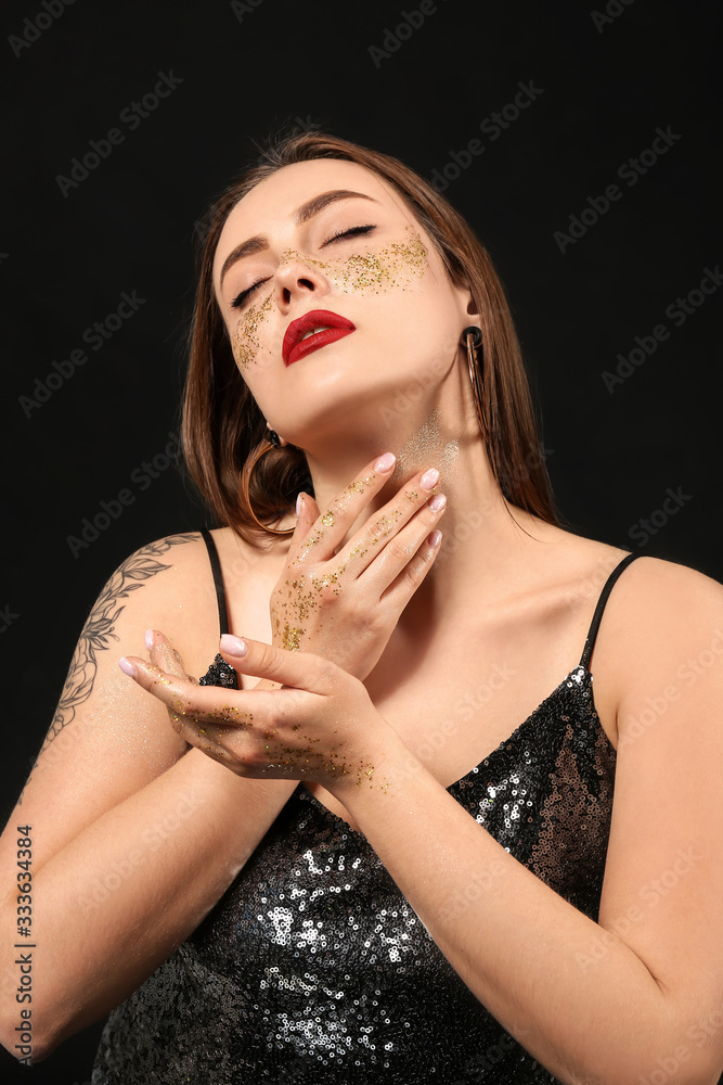 Fashionable young woman with glitters on her body against dark background