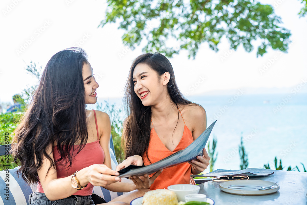 Two young cute Asian best friend women sitting in outdoor restaurant ordering food for lunch. Girls 