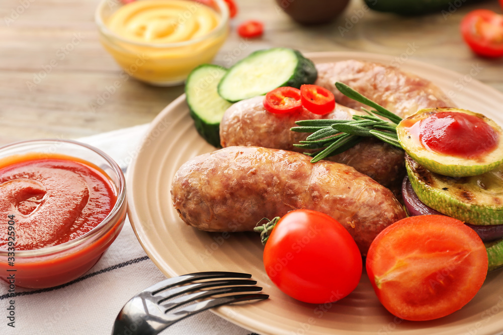 Plate with tasty grilled sausages, vegetables and sauce on table