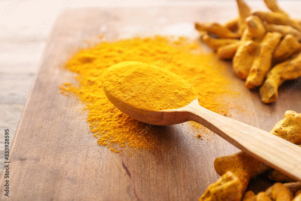 Spoon with aromatic turmeric on wooden board