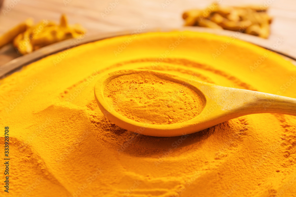 Spoon with aromatic turmeric on table, closeup