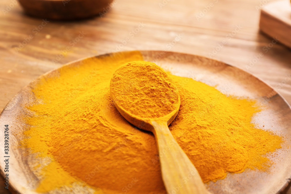 Plate with aromatic turmeric on wooden background