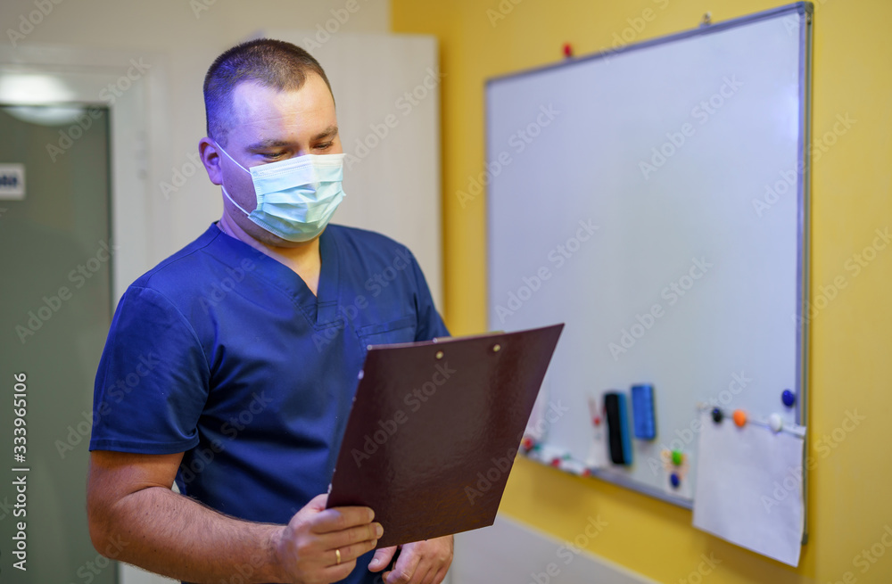 Serious male surgeon with mask standing in office with folder.