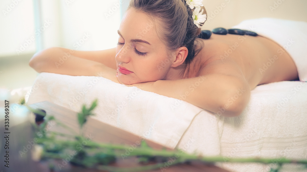 Woman getting hot stone massage treatment by professional beautician therapist in spa salon. Luxury 