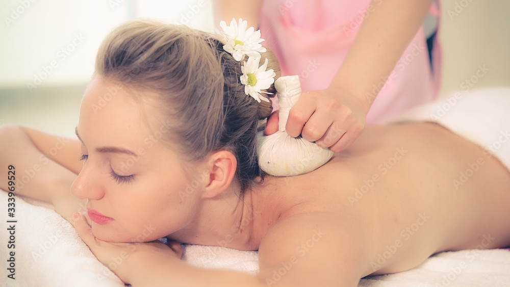 Massage therapist holds a herbal compress to do treatment to woman lying on spa bed in a luxury spa 