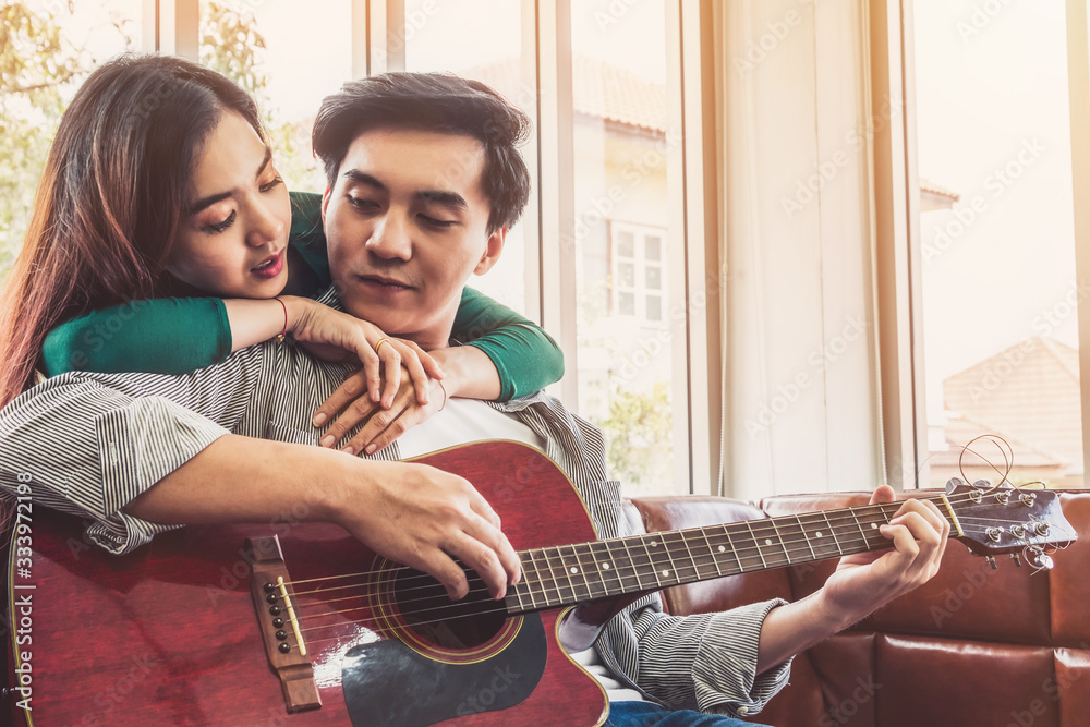 Young Asian Couple Plays Guitar and Sing Song in Living Room at Home Together. Music and Lifestyle c