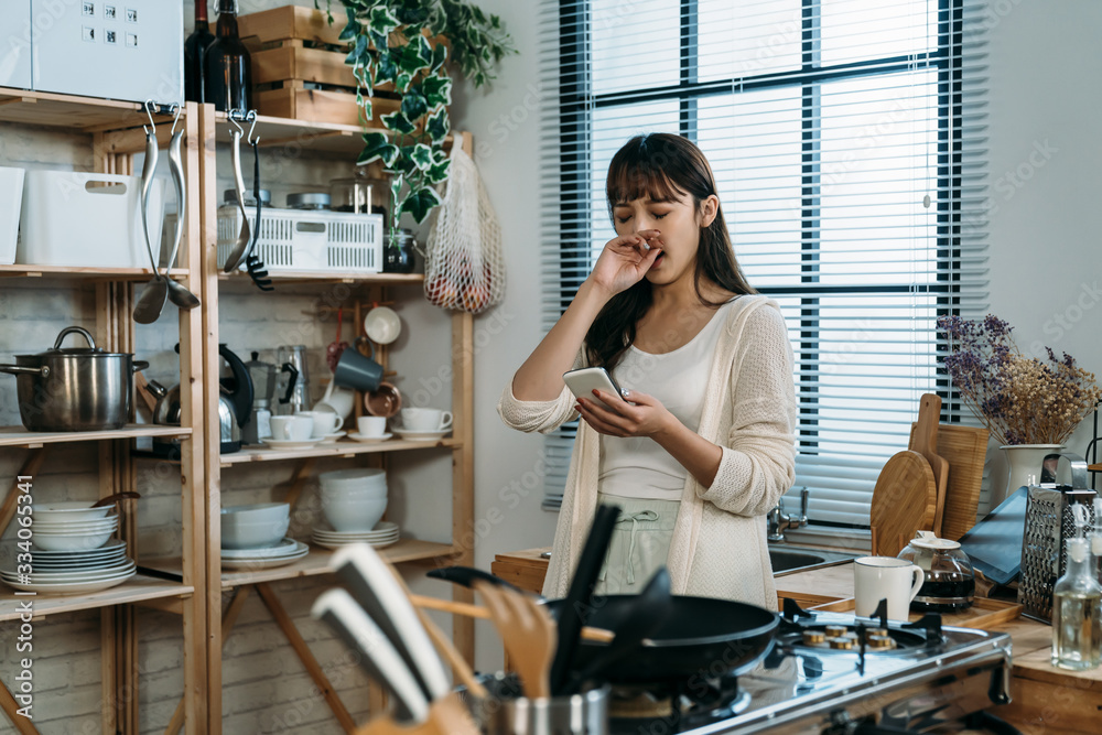 A tired Chinese woman just wake up yawning and reply the message to her friend in the kitchen, enjoy