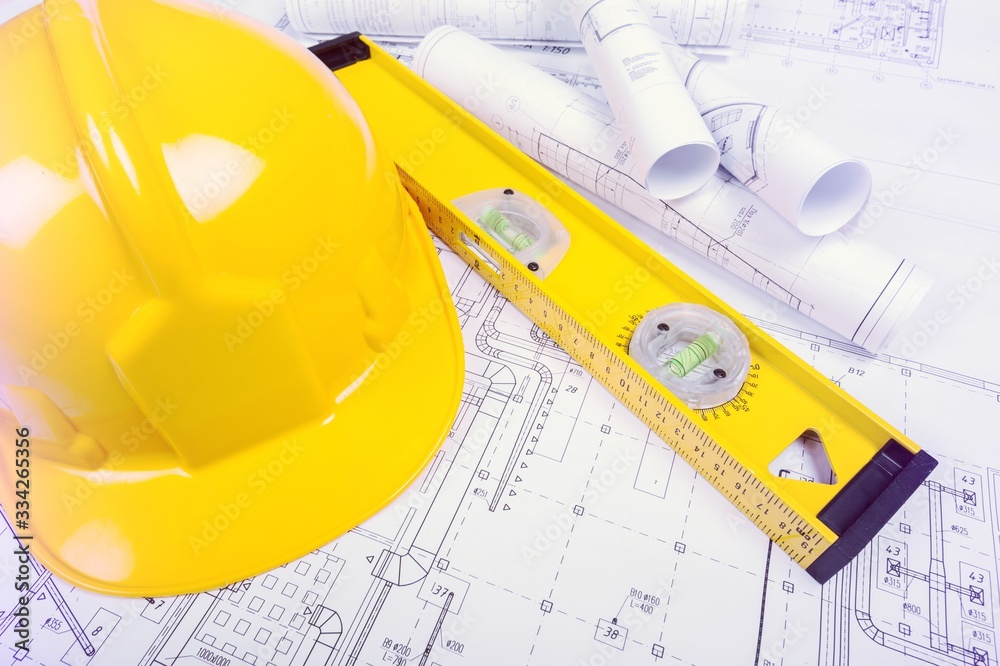 Paper blueprints, a yellow hardhat and tools