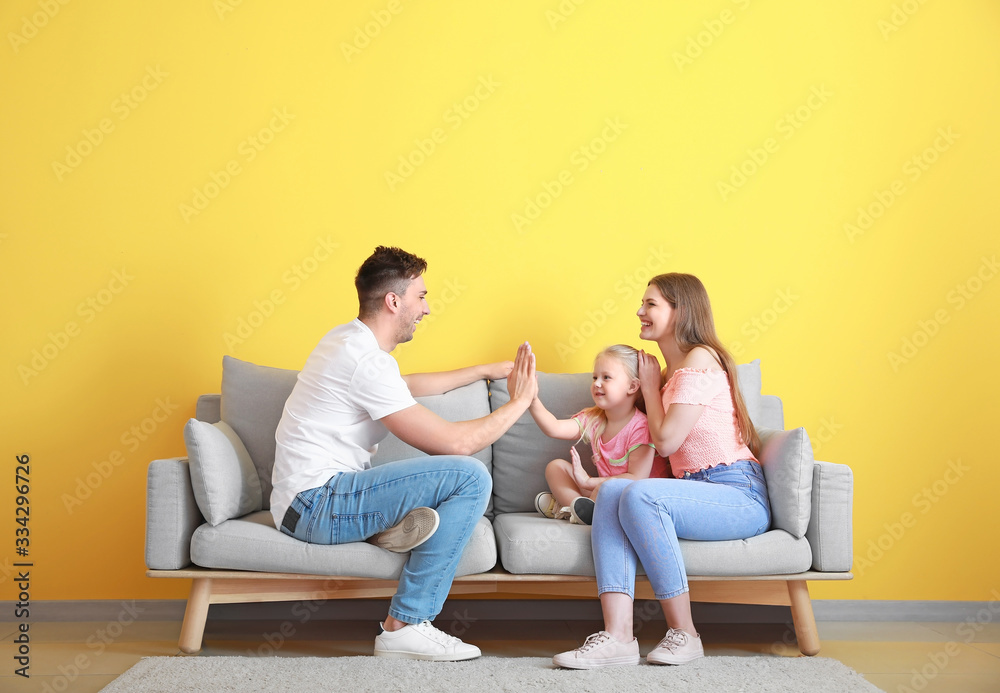 Happy young family playing while sitting on sofa near color wall