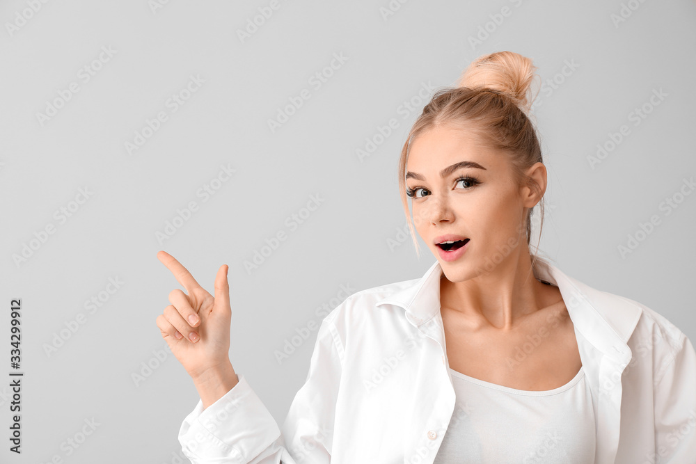 Beautiful young woman showing something on grey background